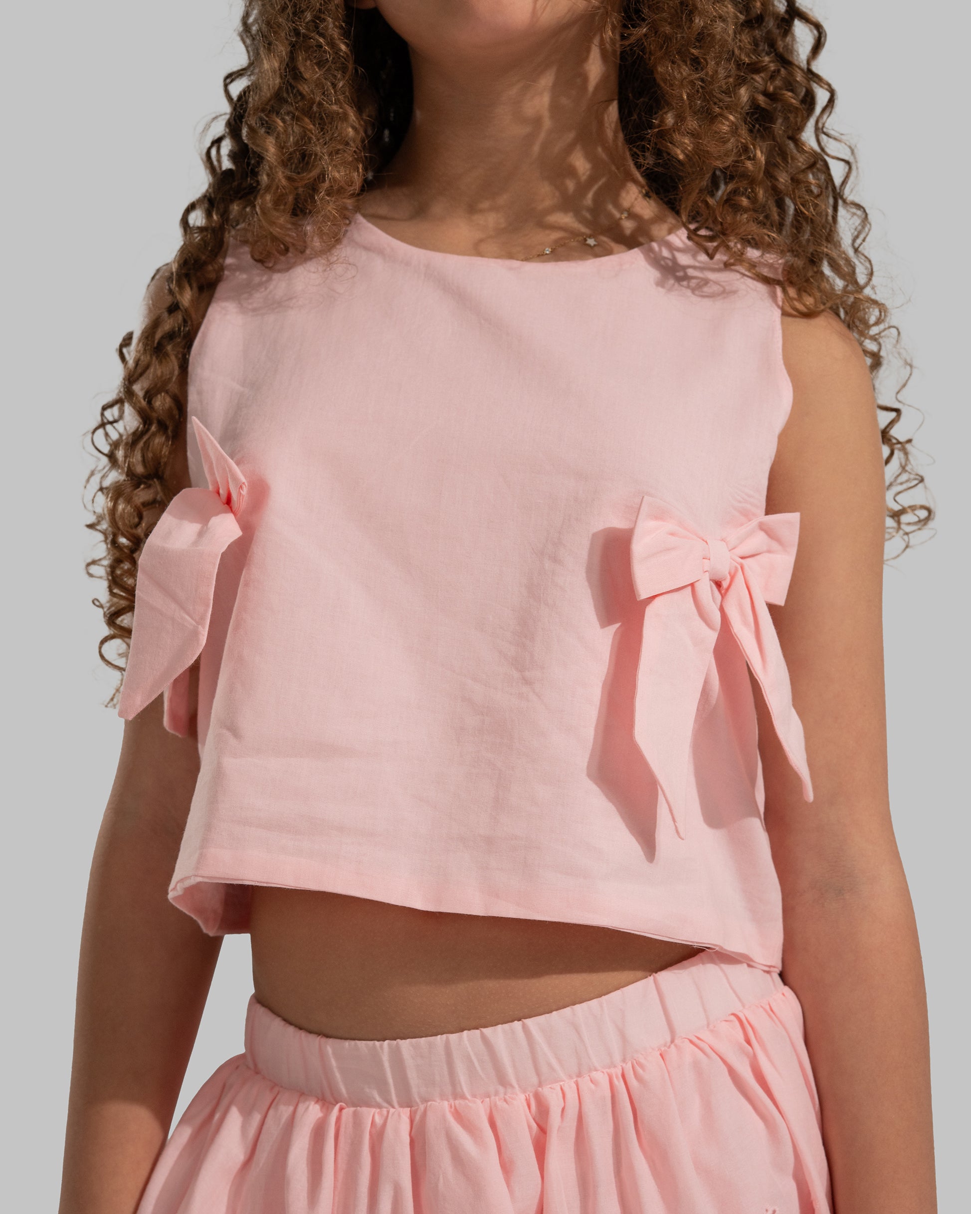 Sleeveless round neck top featuring decorative bows on the sides.